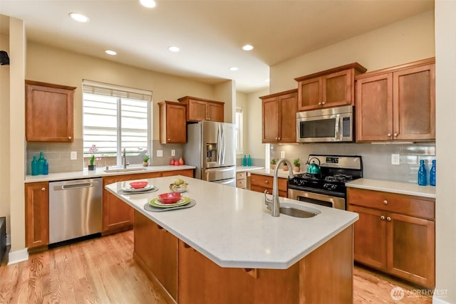 kitchen featuring light countertops, appliances with stainless steel finishes, a center island with sink, and brown cabinets