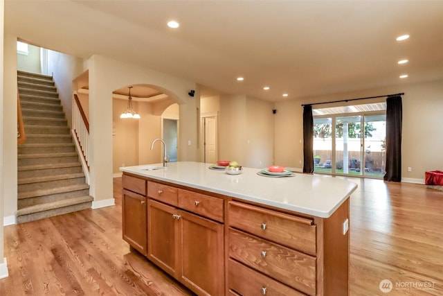 kitchen with arched walkways, a kitchen island with sink, recessed lighting, a sink, and light wood-style floors