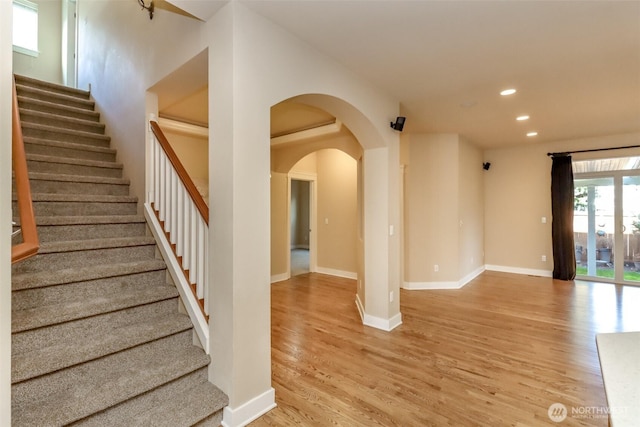 interior space with baseboards, arched walkways, stairway, light wood-style floors, and recessed lighting