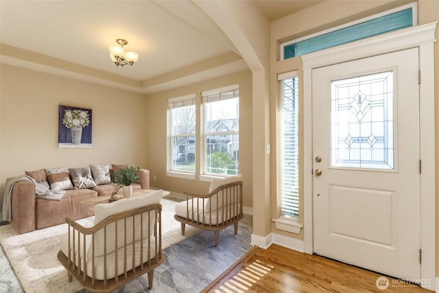 foyer entrance featuring arched walkways, a tray ceiling, baseboards, and wood finished floors