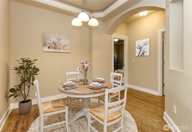 dining space featuring baseboards, arched walkways, wood finished floors, and ornamental molding