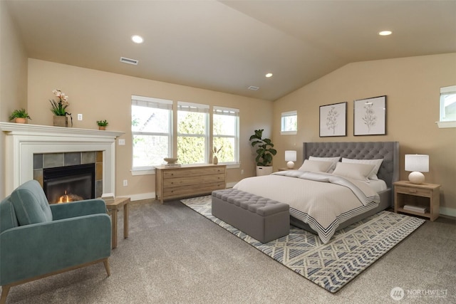 carpeted bedroom featuring a tile fireplace, visible vents, vaulted ceiling, and multiple windows