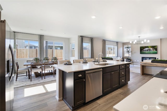 kitchen with a center island with sink, stainless steel appliances, decorative light fixtures, light hardwood / wood-style floors, and sink