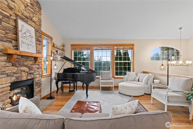 living room with an inviting chandelier, vaulted ceiling, a stone fireplace, light wood-type flooring, and baseboards