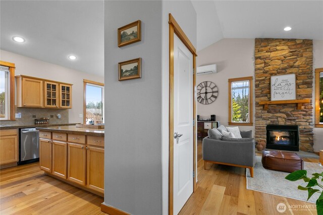 kitchen featuring dark countertops, glass insert cabinets, an AC wall unit, a stone fireplace, and dishwasher