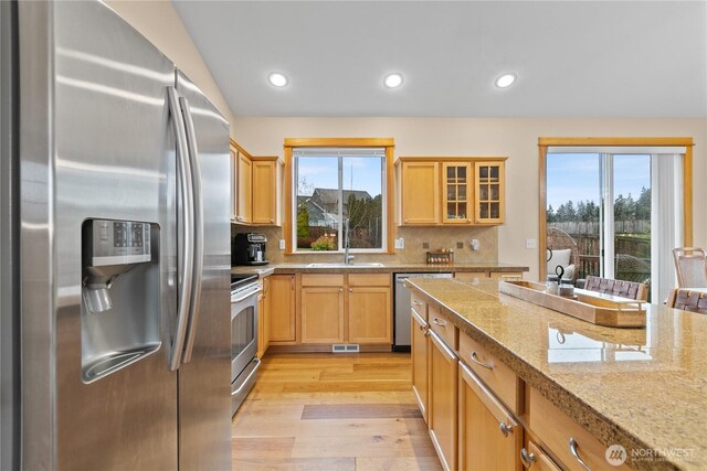 kitchen with tasteful backsplash, glass insert cabinets, appliances with stainless steel finishes, light wood-type flooring, and recessed lighting