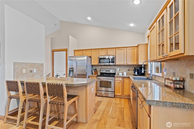 kitchen featuring glass insert cabinets, appliances with stainless steel finishes, vaulted ceiling, a kitchen bar, and a sink