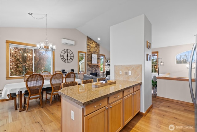 kitchen featuring a wall mounted air conditioner, a notable chandelier, a stone fireplace, and light wood finished floors