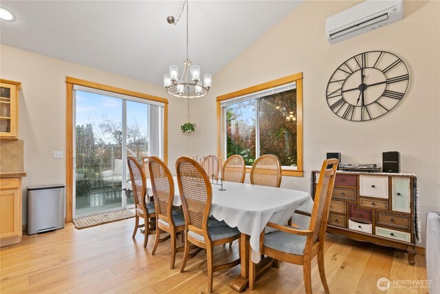 dining area with lofted ceiling, a wall unit AC, a chandelier, and light wood-style flooring