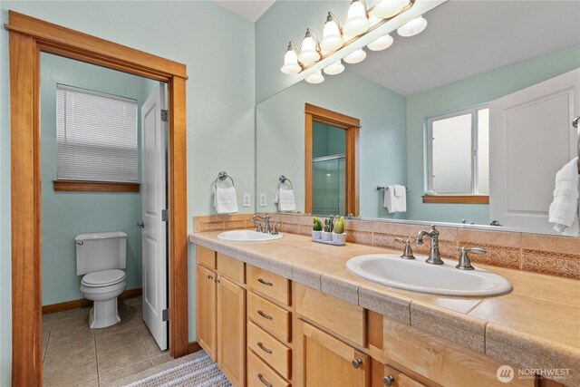 bathroom with double vanity, a sink, toilet, and tile patterned floors