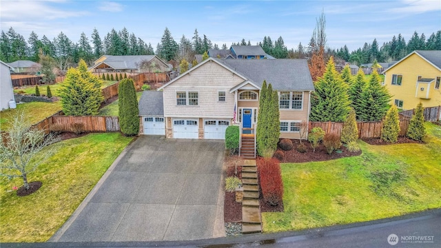 raised ranch featuring a garage, fence, concrete driveway, stairway, and a front yard