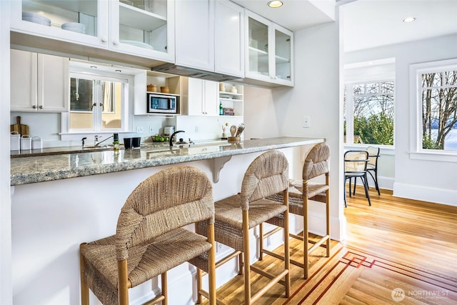 kitchen featuring light wood-style flooring, stainless steel microwave, stone countertops, and white cabinetry