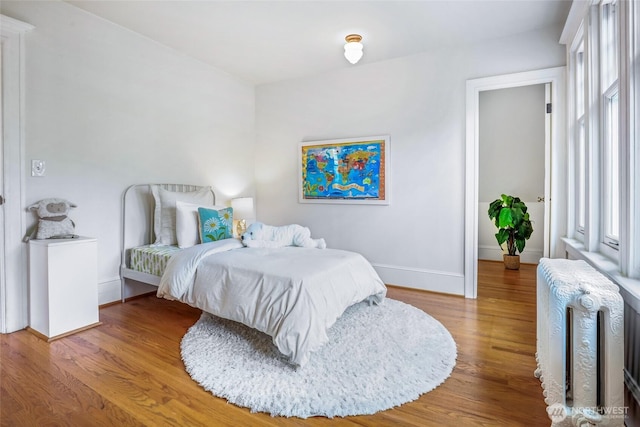 bedroom with radiator, baseboards, and wood finished floors