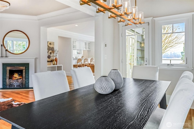 dining room with ornamental molding, a warm lit fireplace, a chandelier, and wood finished floors