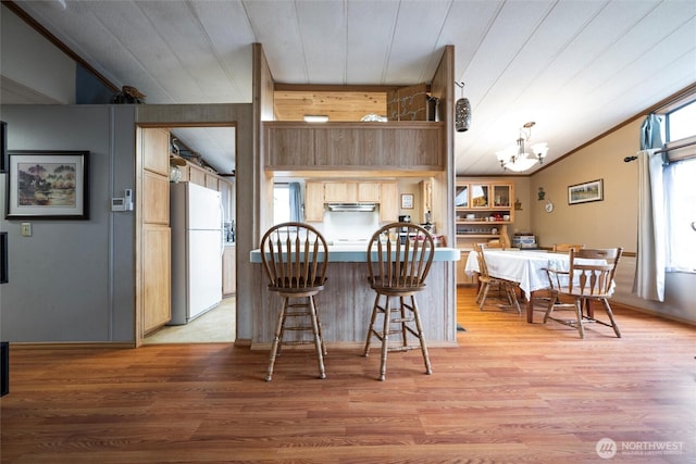 kitchen featuring freestanding refrigerator, vaulted ceiling, light wood-type flooring, under cabinet range hood, and a notable chandelier