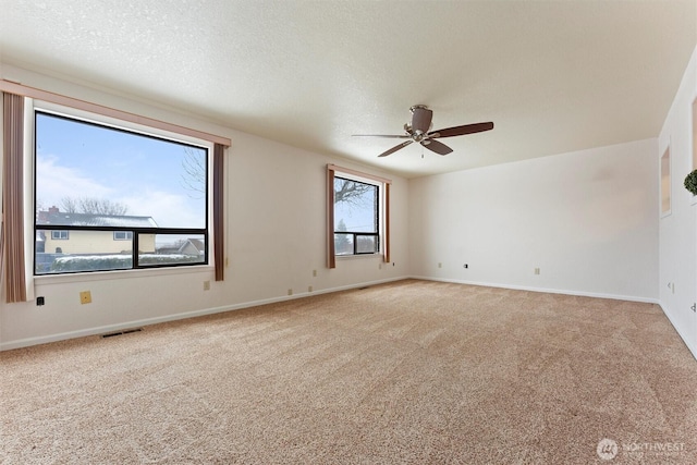 spare room with light colored carpet, visible vents, a textured ceiling, and baseboards