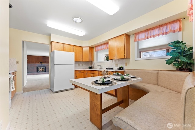 kitchen with light floors, light countertops, backsplash, freestanding refrigerator, and a glass covered fireplace