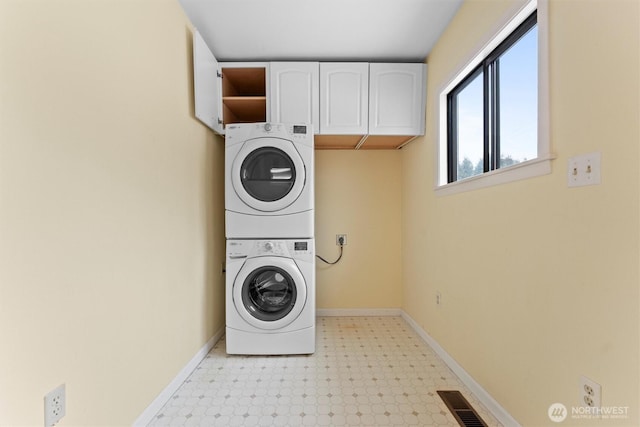 clothes washing area with cabinet space, visible vents, baseboards, light floors, and stacked washing maching and dryer