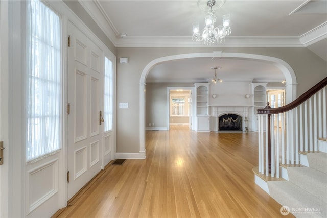 entrance foyer featuring baseboards, light wood-style flooring, a fireplace with flush hearth, ornamental molding, and stairs