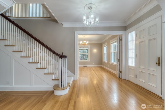 entrance foyer featuring a chandelier, ornamental molding, light wood-style flooring, and a decorative wall