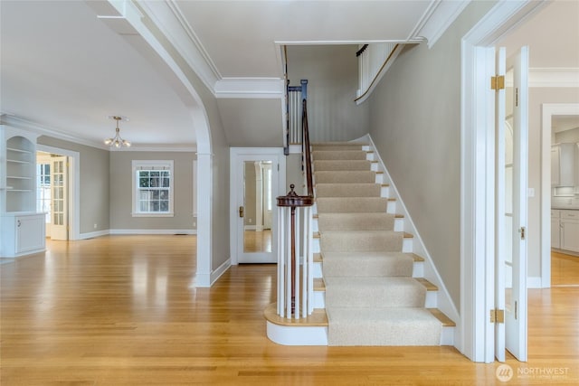 staircase featuring baseboards, ornamental molding, arched walkways, and wood finished floors