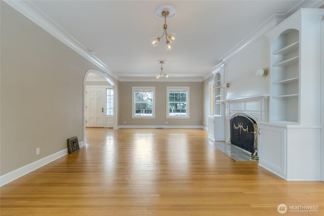 unfurnished living room featuring built in features, a chandelier, crown molding, and light wood finished floors