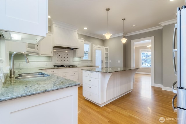 kitchen featuring light stone counters, stainless steel appliances, a sink, a kitchen island, and white cabinetry