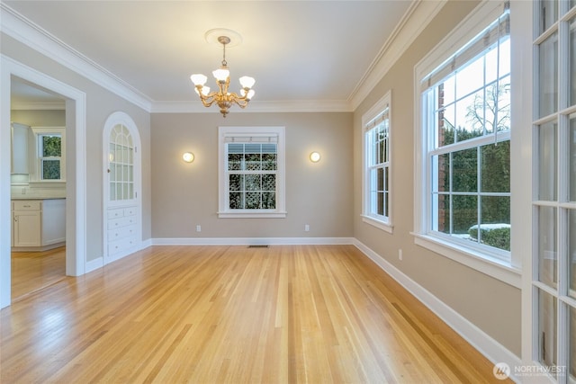 empty room with baseboards, light wood finished floors, an inviting chandelier, and crown molding