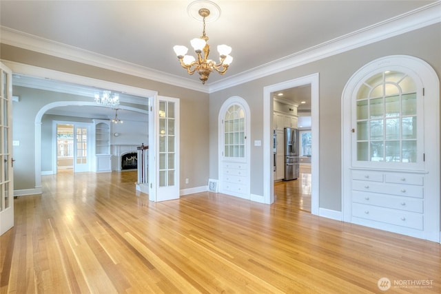 unfurnished dining area with a chandelier, a fireplace, french doors, ornamental molding, and light wood-type flooring