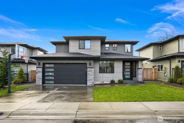 prairie-style home featuring an attached garage, a shingled roof, fence, concrete driveway, and a front lawn