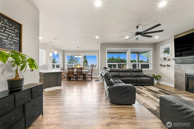 living room featuring a tiled fireplace, light wood-type flooring, baseboards, and recessed lighting