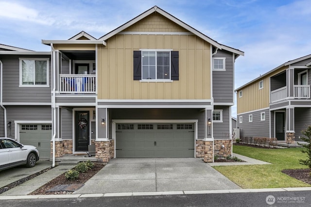 view of front of house with concrete driveway, an attached garage, a front yard, a balcony, and stone siding