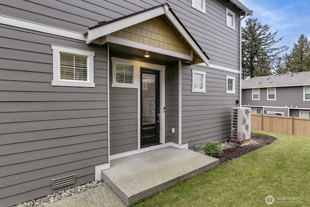 view of exterior entry with central AC unit, fence, visible vents, crawl space, and a lawn