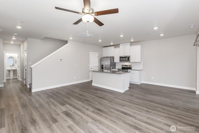 kitchen with an island with sink, appliances with stainless steel finishes, open floor plan, and wood finished floors