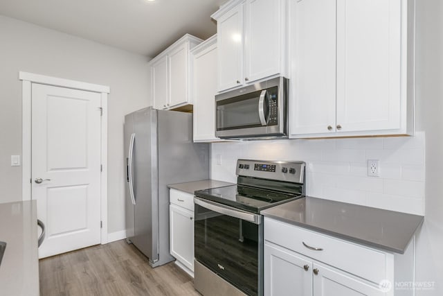 kitchen with light wood-style flooring, stainless steel appliances, white cabinetry, backsplash, and dark countertops