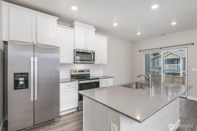 kitchen with wood finished floors, a sink, white cabinetry, appliances with stainless steel finishes, and a center island with sink