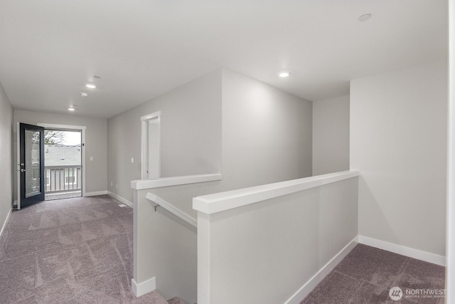 hallway with carpet floors, baseboards, and an upstairs landing