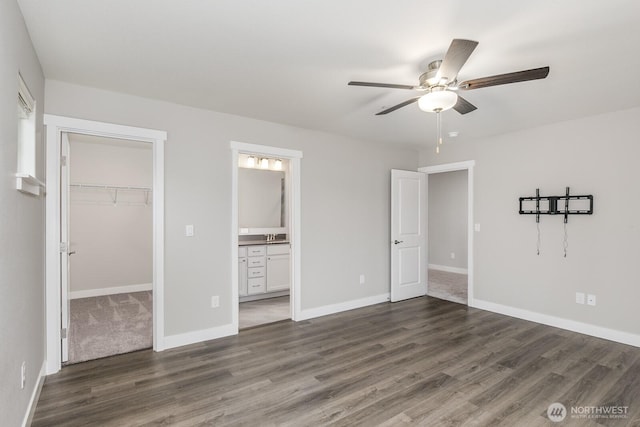 unfurnished bedroom featuring a walk in closet, a closet, baseboards, and wood finished floors