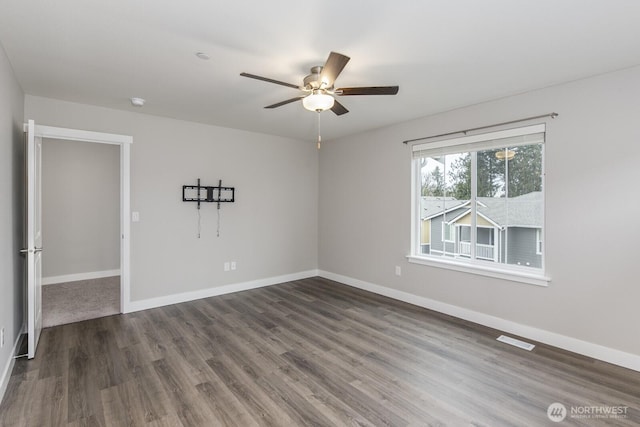 empty room featuring dark wood finished floors, visible vents, and baseboards