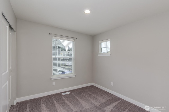 spare room featuring dark carpet, visible vents, and baseboards