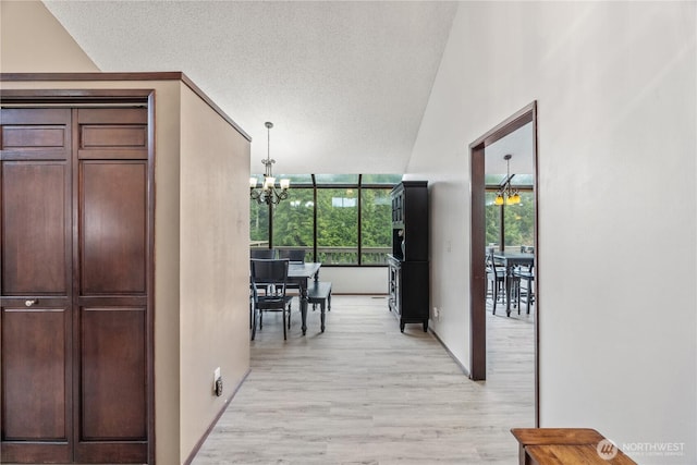 hall featuring light wood-style floors, a chandelier, and a textured ceiling