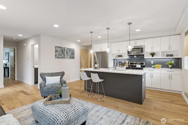 kitchen with stainless steel appliances, a sink, white cabinets, light wood finished floors, and an island with sink