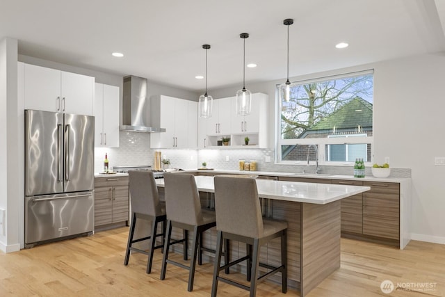 kitchen featuring a kitchen island, a sink, high end fridge, wall chimney exhaust hood, and tasteful backsplash