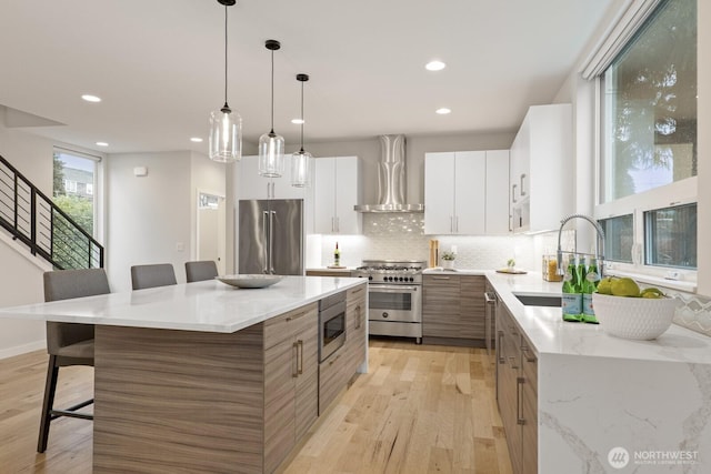 kitchen featuring a breakfast bar area, tasteful backsplash, light wood-style floors, high quality appliances, and wall chimney exhaust hood