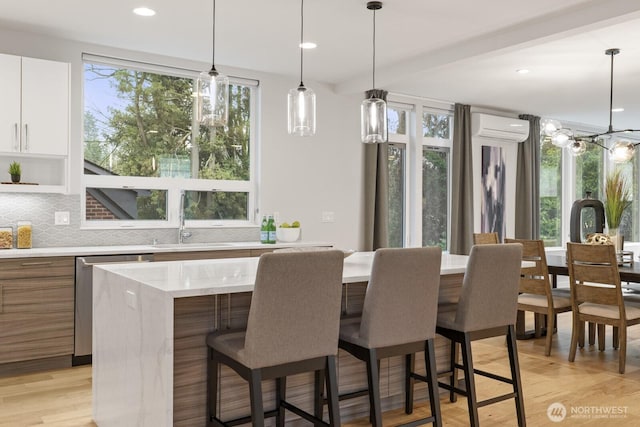 kitchen with decorative backsplash, a sink, an AC wall unit, light wood-style floors, and stainless steel dishwasher