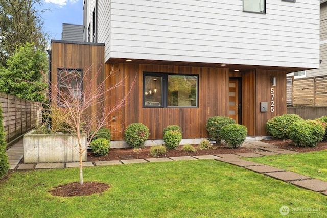 view of exterior entry featuring fence and a lawn