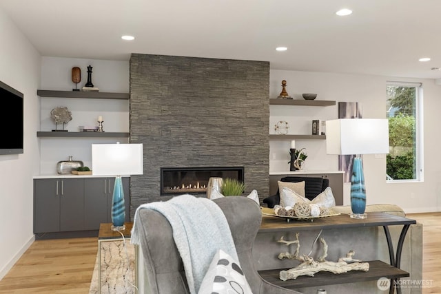 living area with baseboards, a stone fireplace, light wood-style flooring, and recessed lighting