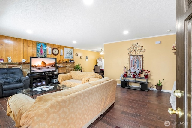 living area featuring wooden walls, dark wood-style flooring, ornamental molding, and a textured ceiling