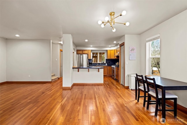 kitchen featuring light wood-type flooring, dark countertops, stainless steel appliances, an inviting chandelier, and brown cabinetry