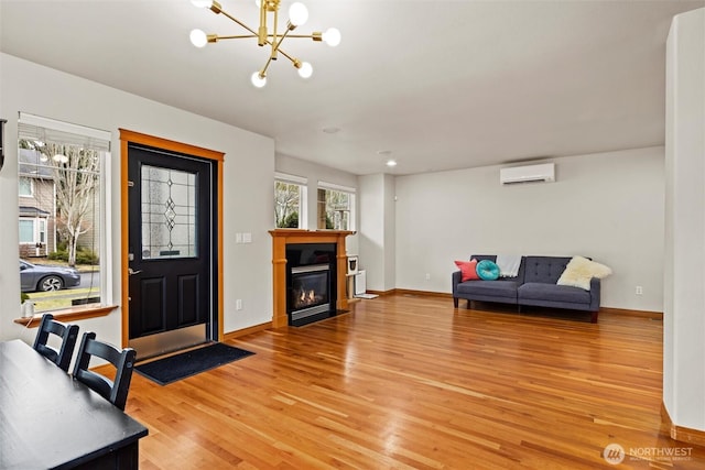 living room featuring a fireplace with flush hearth, light wood-style flooring, a wall unit AC, baseboards, and a chandelier